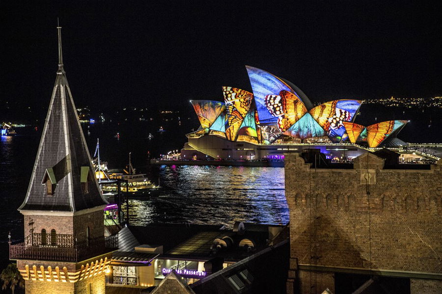 The Sydney Opera House lit up in multi-coloured lights against a dark night sky