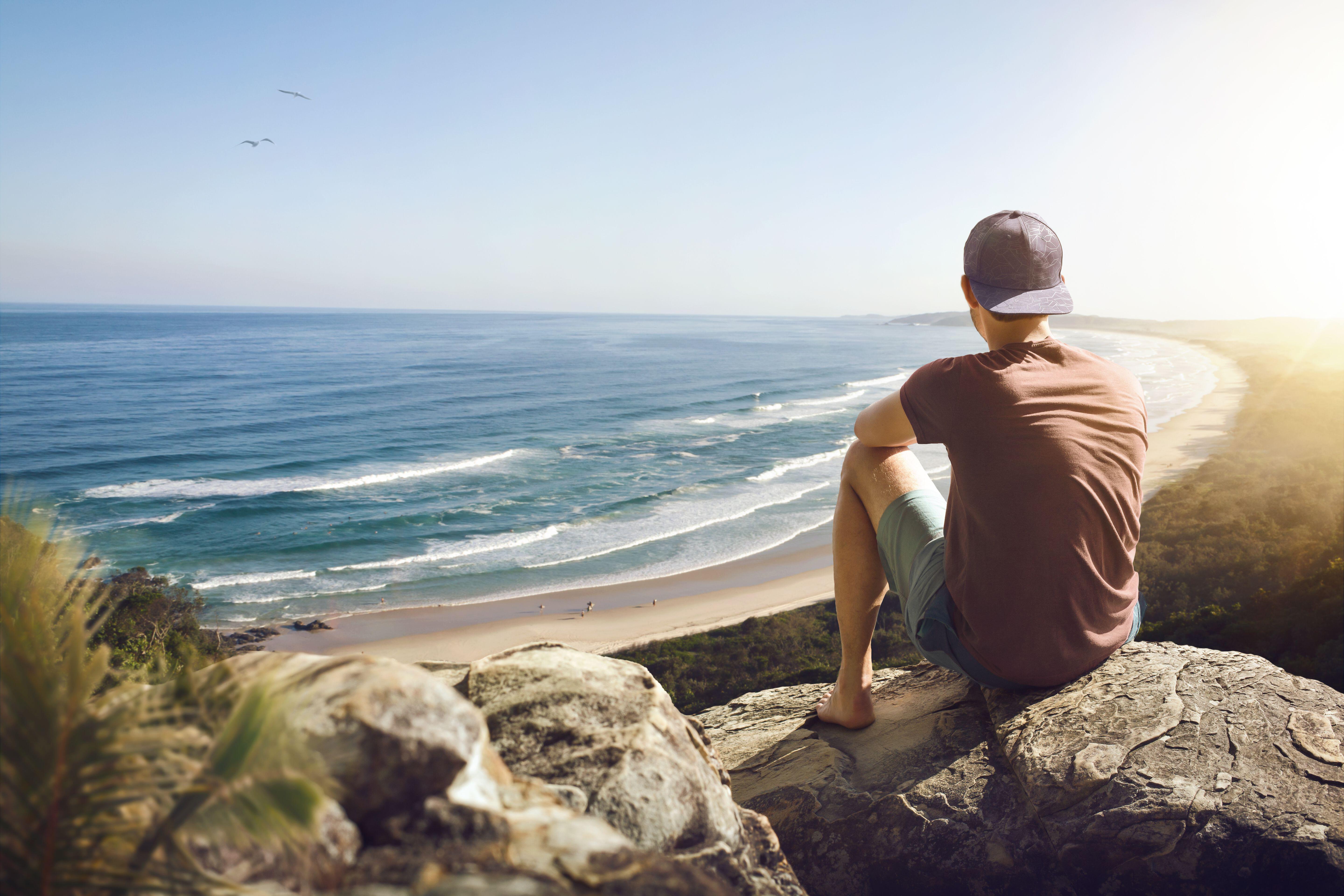 Young man sitting on a rock above a beautiful coastline, Australia
