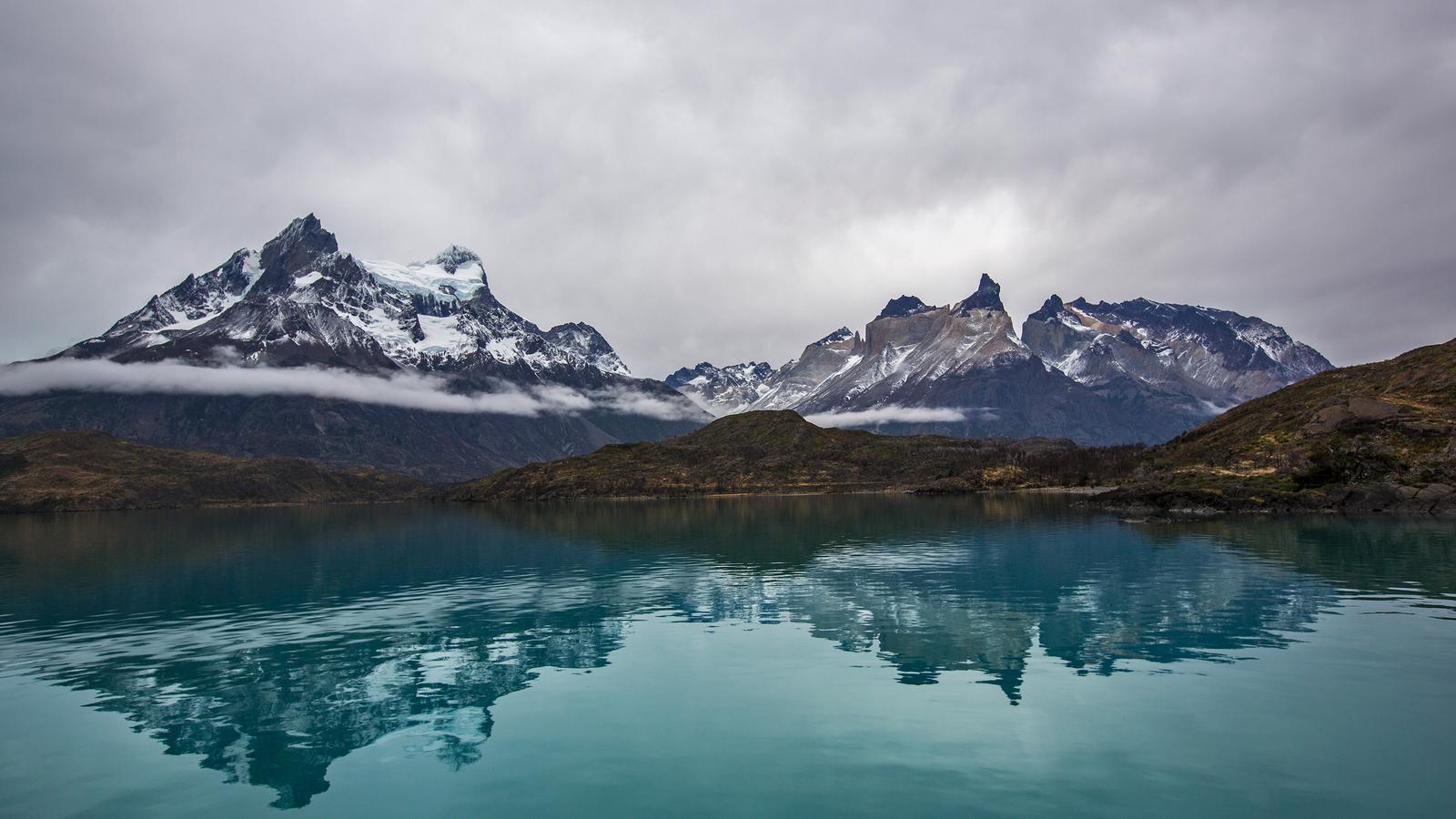Looking across the emerald green water to the snow- capped rocky mountains in the distance on a bright morning in Torres del Paine National Park, Chile
