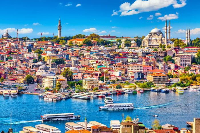 Touristic sightseeing ships in Golden Horn bay of Istanbul and mosque with Sultanahmet district against blue sky and clouds.
