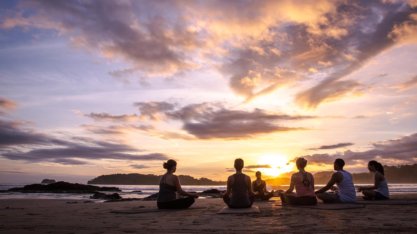 A group enjoy an early morning yoga session amongst the lush green leaves on a bright morning in La Fortuna, Costa Rica