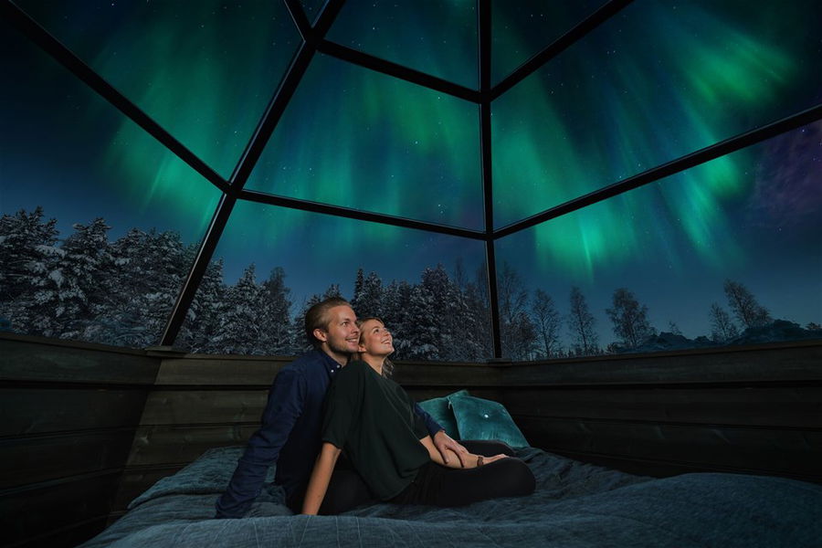 a couple looking at the northern lights through a glass igloo in finland