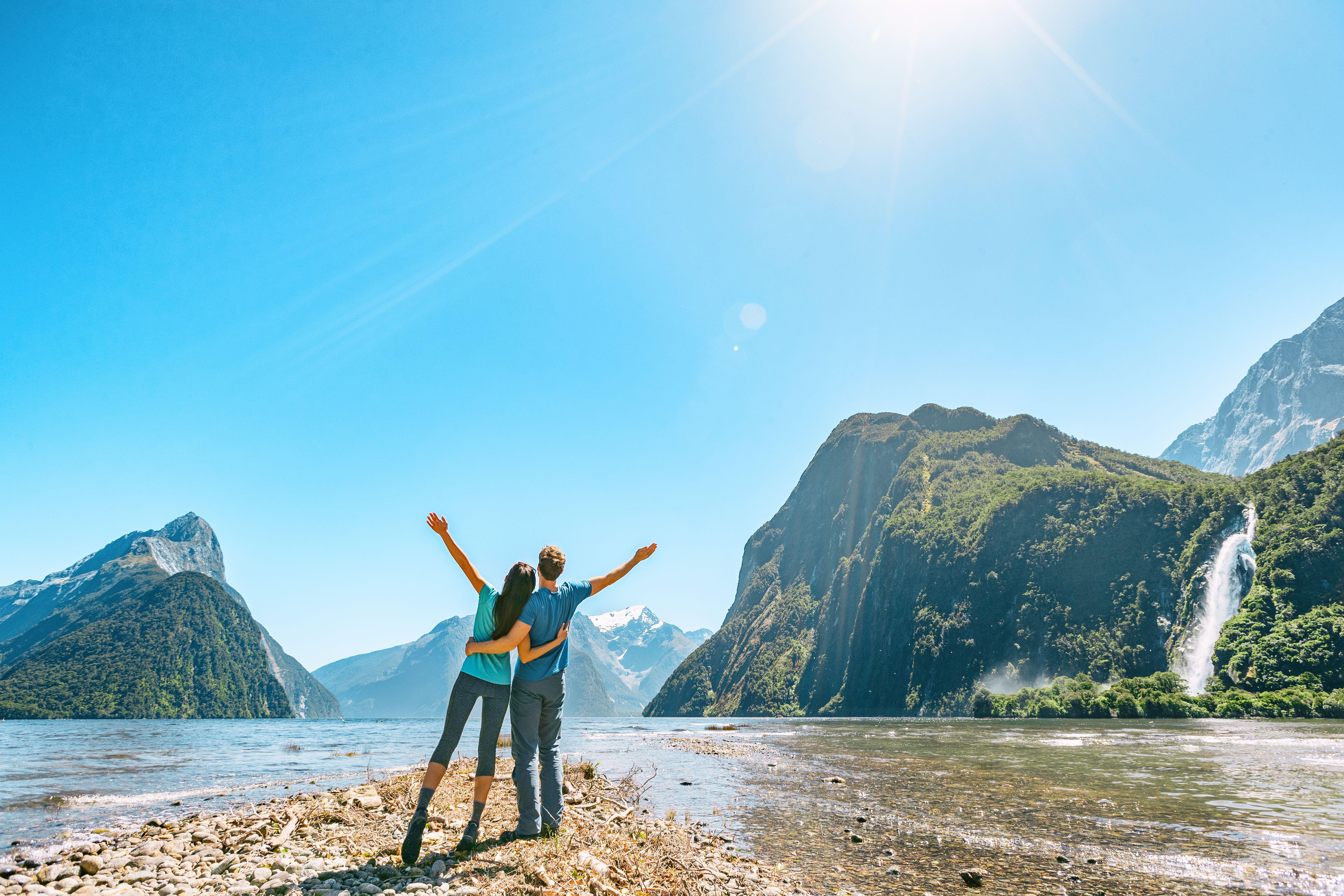 Outdoor couple happy with arms outstretched in Milford Sound, New Zealand