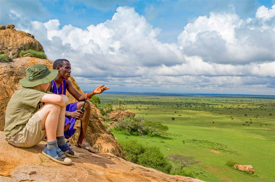 A Maasai guide describes the landscape to a boy on a family safari. Kenya