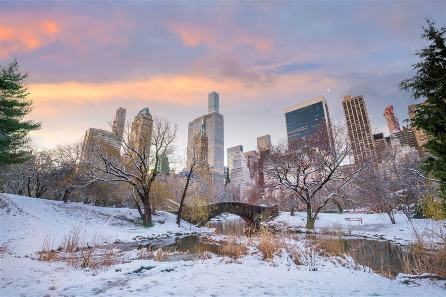 Gapstow Bridge in Central Park covered in snow with skyscrapers in the background, New York