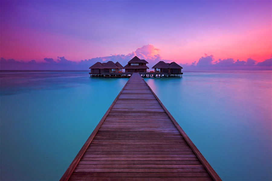 A jetty leading to overwater villas at sunset in the Maldives