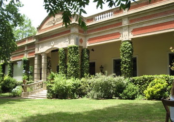 The grand exterior of Estancia El Ombu de Areco with terracota bricks and grand pillars covered in ivy overlooking the lawn