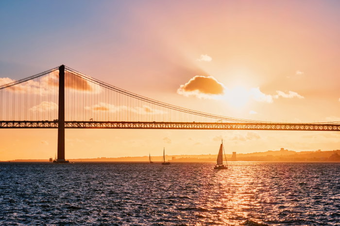 View of 25 de Abril Bridge famous tourist landmark of Lisbon connecting Lisboa and Almada on Setubal Peninsula over Tagus river with tourist yacht silhouette on sunset. Lisbon, Portugal - lisbon, sunset, river, tagus, boat, portugal, sea, view, water, travel, city, landscape, clouds, sun, silhouette, europe, bridge, yacht, cityscape, tourism, transportation, portuguese, traffic, transport, suspension bridge, vessel, boats, tagus river, yachts, suspension, landmark, lisboa, almada, 25 de abril bridge, 25 de abril, 25th of april bridge, attraction, dramatic sky, dramatic sunset, european, famous, ponte, ponte 25 de abril, tejo, tourist boat