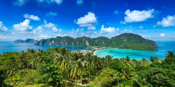 Phenomenal panoramic view of Phi Phi island Thailand showing lush green mountains and turquoise water in the background with forest and beach in the foreground.