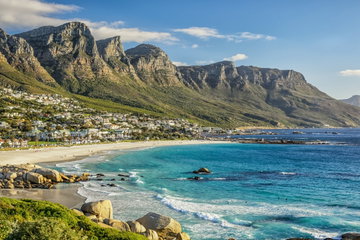 Mountains with fynbos in the foreground and the turquoise ocean to the right, with a sunny, cloudy sky, Cape Town