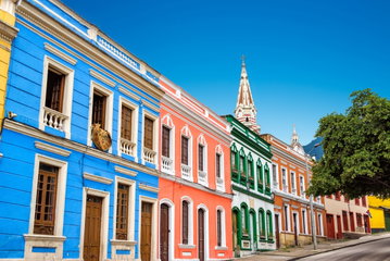 Brightly coloured historical houses with balconies and wooden shutters slope upwards on a hilly street in La Candelaria district, Bogota, Colombia