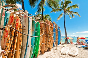 A rack of colourful surfboards stacked on the white sands of Waikiki Beach next to palm trees on a sunny day. Honolulu, Oahu, Hawaii, USA 