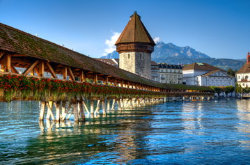 Chapel Bridge across the river Reuss in Lucerne, Switzerland, with lakeside buildings in the background set against a blue sky