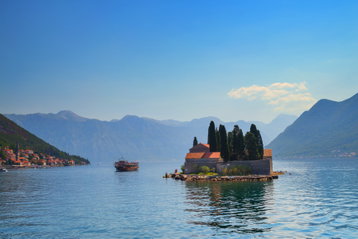 Buildings sit crammed on tiny St. George Island in a glistening lake surrounded by mountains in Bay of Kotor, Montenegro