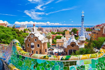 Close up of the mosaics of the wall at Gaudi’s Parc Guell, overlooking the trees of the park and views of Barcelona, Spain.