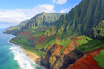 Aerial view of rugged, tree-lined mountains meeting the ocean at Na Pali Coast State Wilderness park on a sunny day, Kauai, Hawaii, USA