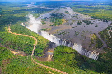 Aerial view of the towering Victoria Falls spewing mist into the air surrounded by lush green wetlands, Zimbabwe-Zambia border
