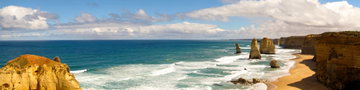 The striking Twelve Apostles interrupt the rough waves below, leading towards the golden sand and rugged cliffs of the Great Ocean Road, Australia