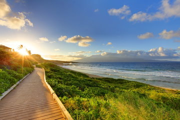 A boardwalk cutting through the shrubbery that both run parallel to a deserted sandy beach, with waves gently breaking and the sun setting, Maui, Hawaii, USA