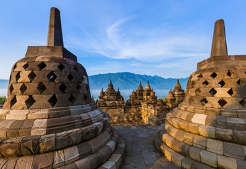 A couple of stone stupas at Borobadur temple with more in the distance against a mountainous backdrop in East Java, Indonesia.