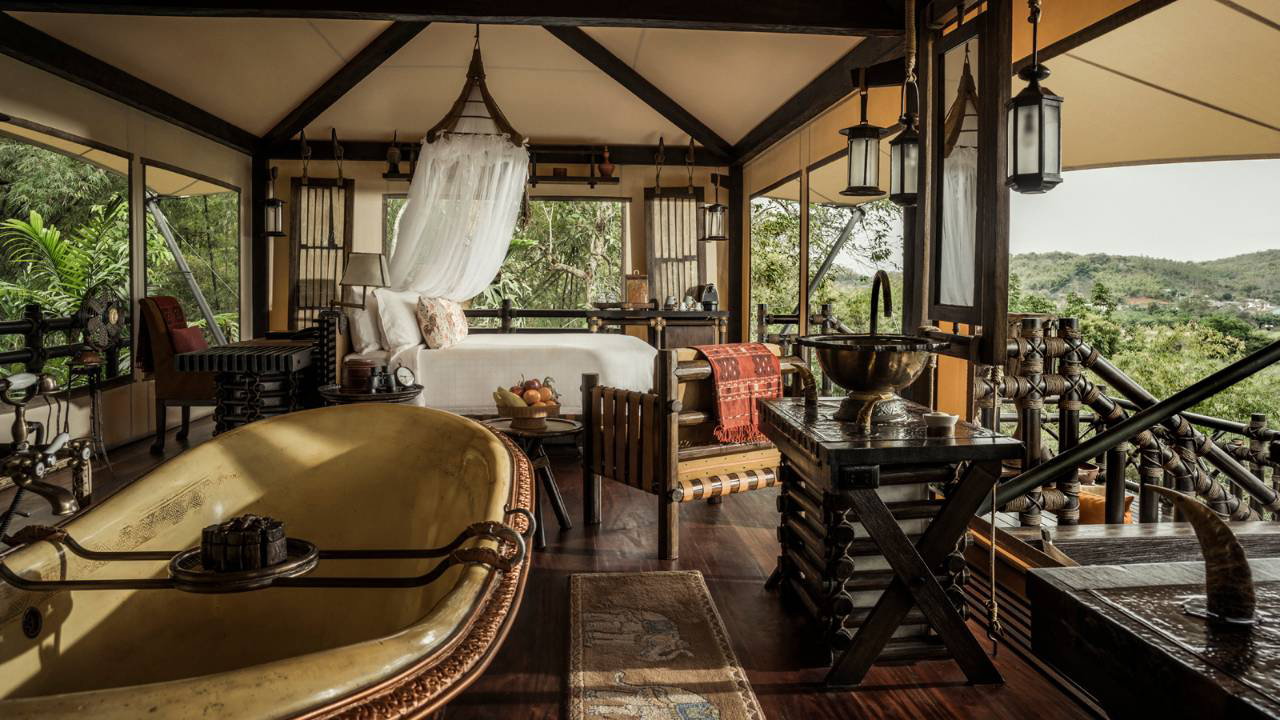 An open-sided luxury tent at the Four Seasons Golden Triangle, with a roll-top bath and dark wood furniture overlooking dense forest, Thailand