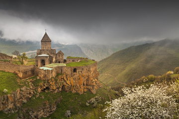 Ancient Tatev Monastery perches on a rocky outcrop high in the mountains on a dark cloudy day in Armenia