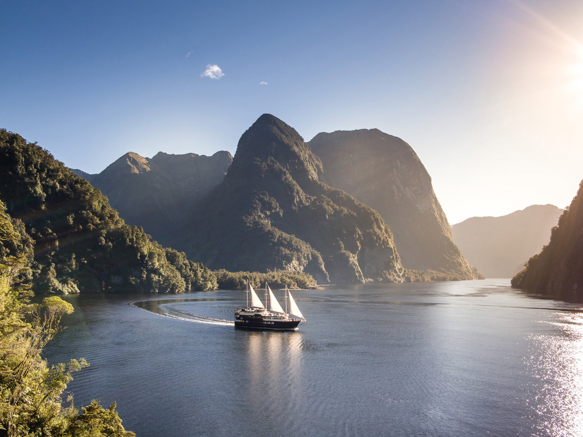 Boat sailing the calm waters surrounded by towering banks and forest, 1 Night Doubtful Sound Cruise, Queenstown, New Zealand.