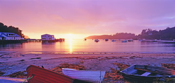 A rural deserted beach at sunset, hypnotising rays of pink mirror across the sea, fishing boats float aimlessly, Halfmoon Bay, New Zealand