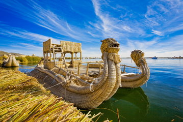 Two totora reed boats on the deep blue Lake Titicaca tied to a floating island by rope, with the lake merging with the blue sky on the horizon