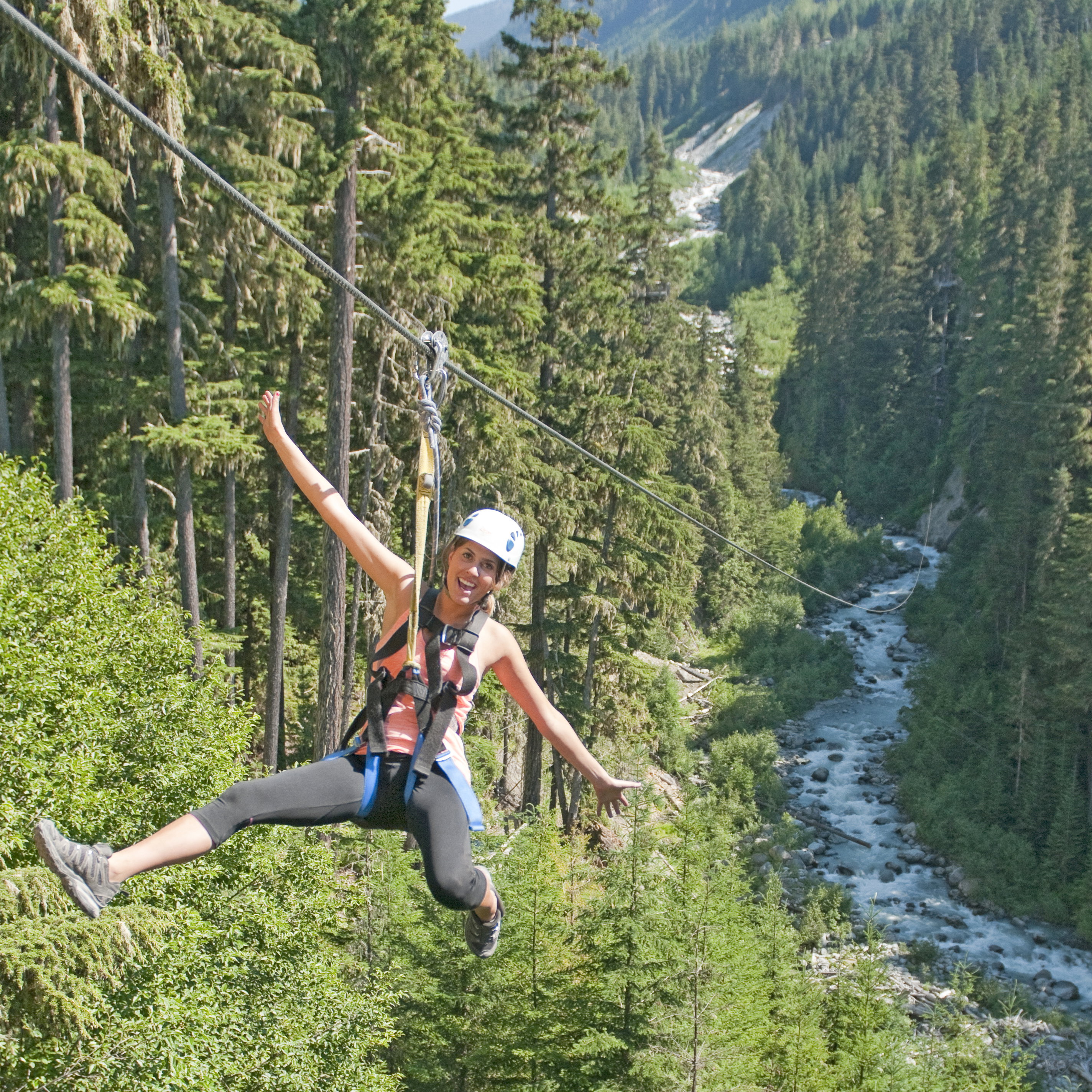 Zipliner soaring high above a fast flowing river and forest, on Whistler Zipline Eagle Tour, British Columbia, Canada