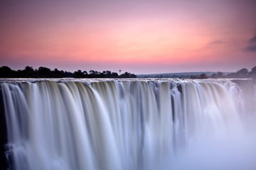 A close-up of the spectacular Victoria Falls at sunset, the white spray contrasts with the pink dreamy sky, Zambia