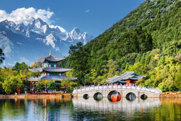 Snow-capped peaks loom over the mountainous Lijiang, China, where traditional tiered buildings and bridges line the river