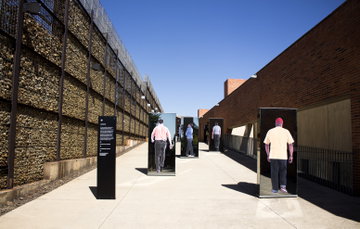 The entrance to the Apartheid Museum, Johannesburg, South Africa with poignant images of various figures walking ahead along a laneway enclosed by brick