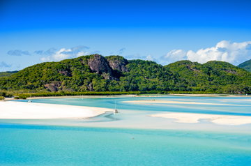Rich bush-clad mountains tower over the crystal clear pale blue sea, dotted with boats and patches of white sand, Queensland Australia