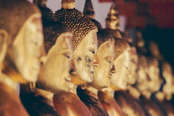 A row of aged golden Buddha statue faces in Bangkok Thailand 