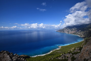 The deep blue sea is framed by a curved bay along the green, rocky coastline of Crete, Greece
