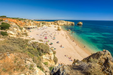 Turquoise waters lapping the golden sands, of Sao Rafael Atlántico, dotted with colourful sun umbrellas. The Algarve, Portugal