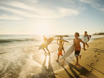 Family with Surfboards running along a sandy beach with the sun shining down on them in California, USA 