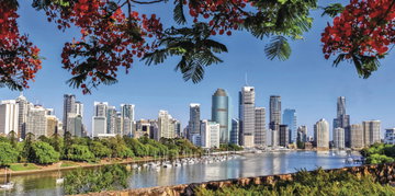 Brisbane’s skyline made up of towering skyscrapers set behind the harbour, dotted with boats and bordered by trees, Australia