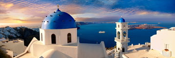 Deep blue domes atop a whitewashed church in Santorini, Greece, sit high above the similarly deep blue ocean, volcanic rock of the Greek island frames the view