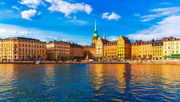 Tall rainbow coloured buildings, mirrored in the glassy water below, with a floating small white sail boat in Sweden.
