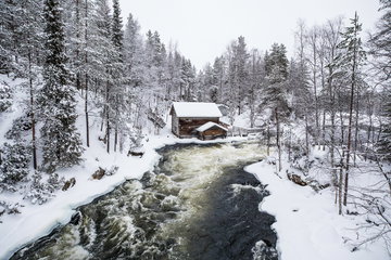 A river rushing through an snowy scene with snow dusted trees and a cosy log cabin at the centre, in Lapland, Finland