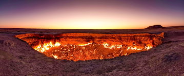 The flames of the Darvaza Crater illuminate the rim against a dusky sky in Derweze, Turkmenistan