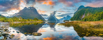 Impressive rugged mountainous scenery partly hidden with the low-lying fluffy clouds, a translucent lake at the forefront, New Zealand