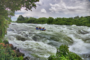 A small blue raft thunders along the cascading white water rapids of the river with dense vegetation lining the banks near Jinja, Uganda