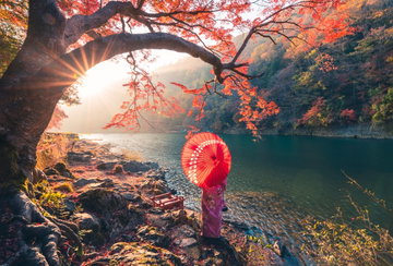 A woman with red umbrella and kimono admiring the view on Katsura river, Japan