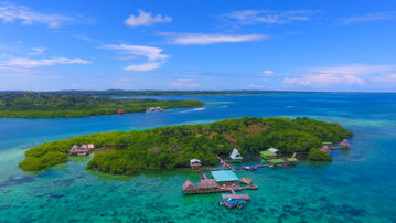 A wide stretch of blue canal flanked by green islands and coastline leading into the sea on a sunny day, Panama