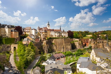 The quaint buildings of Luxembourg City sit on a sheer sided hill top on a sunny day