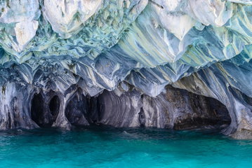 Huge white-blue stalactites are hanging from the roof of a cave reflecting the stunningly blue glacial water below at the Marble Caves, Aysen region, Chile