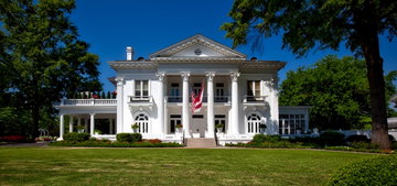 A white antebellum style home sits behind its lawn on a clear sunny day in Montgomery, Alabama, USA